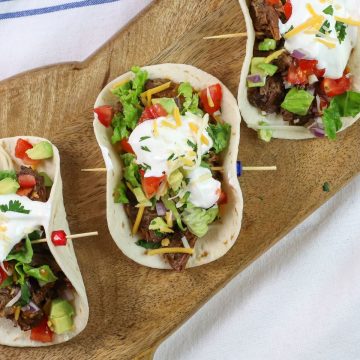 3 barbacoa tacos on a board