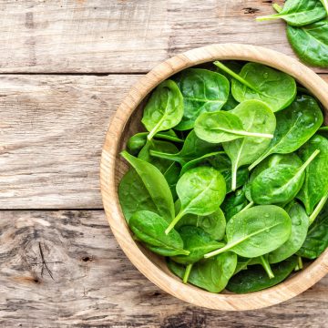 Fresh baby spinach leaves in bowl on wooden background