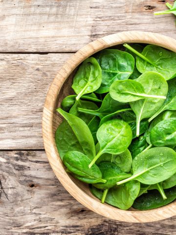 Fresh baby spinach leaves in bowl on wooden background