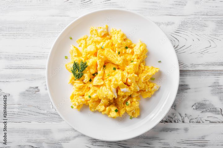Scrambled eggs on white plate over white wooden background.